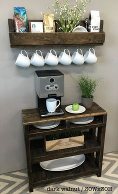 a coffee machine and some cups on a table with a potted plant next to it