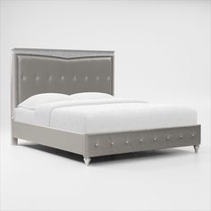 an upholstered bed with white sheets and silver headboard