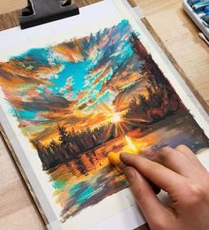 a person is holding a pencil in their left hand and painting on paper with watercolors