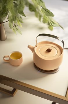 a tea pot and cup sitting on a table next to a vase with green leaves