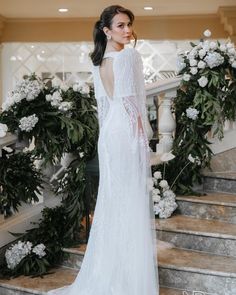 a woman in a white wedding dress standing on some stairs with flowers and greenery