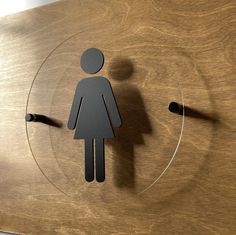 a bathroom sign with a woman's silhouette in the center on a wooden surface