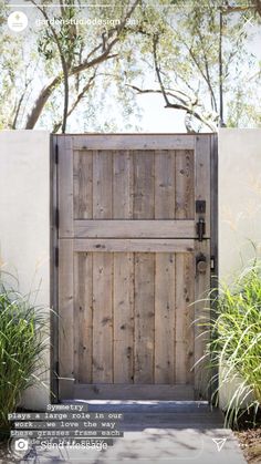 an open wooden door in front of a white wall and some plants on the side