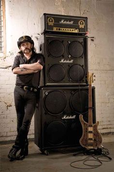 a man standing next to a stack of amps with his arms crossed in front of him