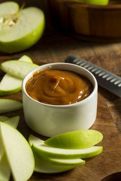 an apple is sliced on a cutting board with caramel sauce in a small bowl