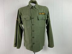 "Vintage 1950s U.S. Army military issue shirt. Made of green cotton. Has two chest pockets, a button down front and patches. About a size medium. Actual measurements are: 44\" at the chest 42\" at the waist 19\" shoulder seam to shoulder seam 23.5\" shoulder seam to cuff 28\" overall length In good condition with large paint stain on right cuff and a couple of small holes on sleeve and spots on back, see pictures." Green Military Style Button-up Shirt, Green Military Button-up Top, 1950s Shirts, Army Shirt, Military Patches, Military Shirt, Army Shirts, Military Patch, Camping Outfits