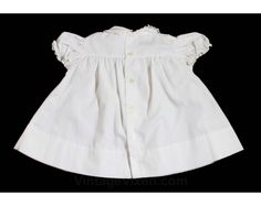 An innocent little frock for your little innocent! This vintage dress has a Peter Pan collar rimmed in lace, puffed sleeves and adorable embroidered daisies to the lapel & dress front. Has two petite decorative buttons at the chest, blue piping along the yoke, and a scalloped skirt. Child's Size 6 Months Measurements Chest 22; Neck to Hem 14 Inches Era 1950s Label '' baby B . . . '' at back neck Materials White cotton broadcloth; baby blue cotton piping; white synthetic lace; white, pale yel White Vintage Dress For Costume Party, Fitted Cotton Baptism Dress For Spring, Cotton Baptism Dress With Short Sleeves For Daywear, Vintage Fitted Baptism Dress For Summer, Fitted Short Sleeve Baptism Dress With Ruffles, Vintage Cotton Dress For Dress-up Occasions, Summer Vintage Fitted Baptism Dress, Short Sleeve Fitted Baptism Dress, White Cotton Vintage Dress With Short Sleeves