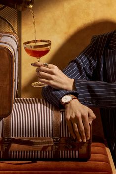 a man in a suit and tie holding a glass of wine next to suitcases