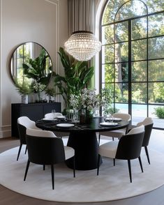 a dining room table with white chairs and a round black table in front of a large window