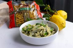 a white bowl filled with pasta next to two lemons and a bag of pasta