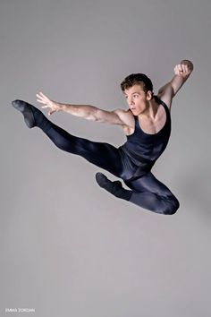 a male ballet dancer in the air with his arms out and legs spread wide open