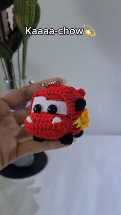 a hand holding a small crocheted keychain with a red car on it