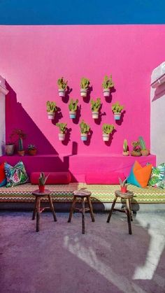 an outdoor seating area with potted plants on the wall and pink walls behind it