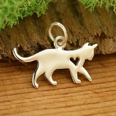 a silver cat charm sitting on top of a wooden table next to a tree branch