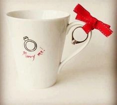 a white coffee cup with a red bow on the handle and merry me written on it