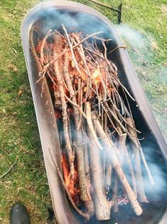 the grill is full of sticks and firewood in it's pan on the grass