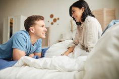 a man laying in bed next to a smiling woman on her stomach, both looking at each other