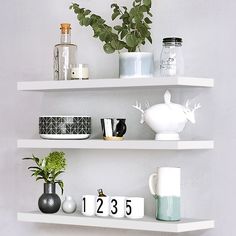 three white shelves with plants and other items on top of each shelf in the corner