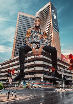 a man sitting on top of a pole in front of a tall building with a sky background