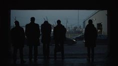 silhouettes of people standing in front of an open garage door at night, with the city skyline behind them