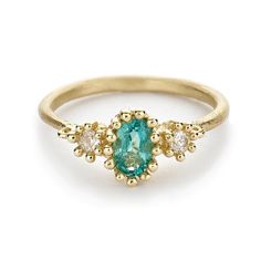 a yellow gold ring with an oval blue stone surrounded by small white and green diamonds