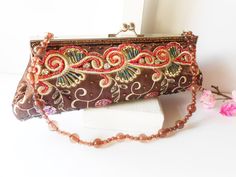 "A dramatic brown beaded evening bag with jewel tone autumn colors. This retro handbag has beautiful jewel tone autumn colors of brown, copper, red and teal. The bag background is brown taffeta with designs of copper and it has a silvertone frame and a kiss lock. The front has swirls of white embroidery with beading in red, teal.  The interior is brown with one pocket. This glamorous autumn clutch includes a chain strap to wear on shoulder and the bag is large enough for an iPhone.  This is a gl Handmade Brown Evening Bag For Party, Brown Embellished Evening Bag, Beaded Brown Evening Bag For Party, Handmade Brown Handheld Evening Bag, Embellished Brown Evening Bag For Party, Brown Handheld Handmade Evening Bag, Elegant Handmade Brown Clutch, Elegant Handmade Brown Evening Bag, Elegant Beaded Brown Bag