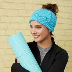 a woman holding a yoga mat and wearing a blue headband smiling at the camera