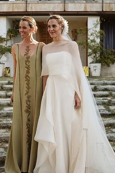 two women standing next to each other in front of a building wearing dresses and veils