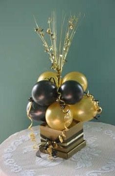 a vase filled with black and gold balloons sitting on top of a white table cloth