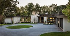 a modern house in the middle of a circular driveway surrounded by trees and grass,