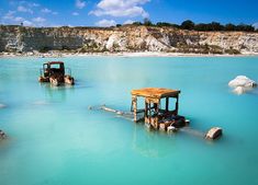 three abandoned boats sitting in the middle of a blue lagoon with cliffs in the background