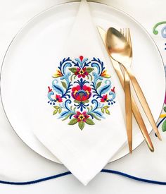 a white plate topped with a gold fork and knife next to a napkin covered in colorful flowers