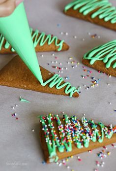 green frosted cookies with sprinkles are on a baking sheet and someone is holding a paper cone