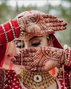 a woman in red and gold holding her hands up to her face with henna on