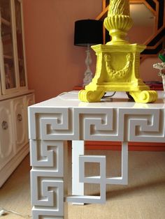 a white table with a yellow vase on top of it next to a mirror and lamp