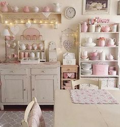 a room filled with lots of pink and white dishes on top of wooden shelves next to a table