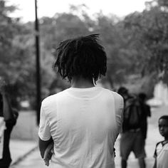 a man with dreadlocks walking down the street in front of other young people