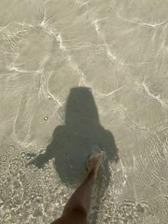 a person standing in shallow water with their shadow on the sand and one foot sticking out