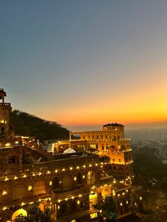 the sun is setting over an old building on top of a hill with lit up lights