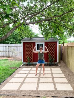 a woman standing in front of a red shed with her arms up and hands behind her head