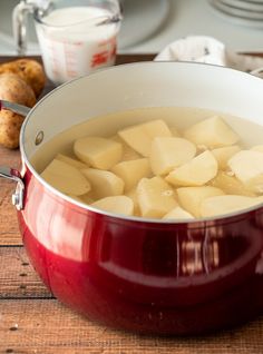 a pot filled with potatoes sitting on top of a wooden table next to plates and utensils