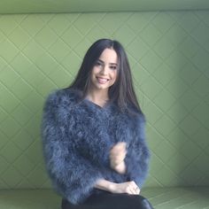 a woman sitting on top of a green bench wearing a blue fur coat over her shoulders