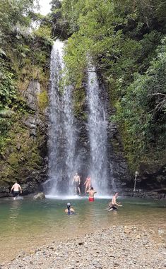 people are swimming in the water near a waterfall