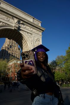 a woman holding up her cell phone in front of an arch