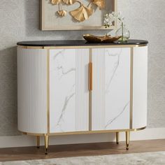 a white cabinet with black top and gold trimmings in front of a painting on the wall