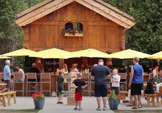 several people are standing outside at an outdoor bar with yellow umbrellas and tables in front of them