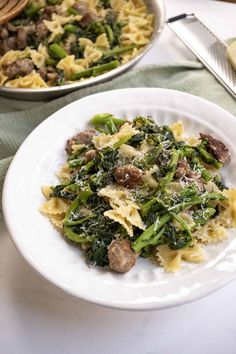 pasta with sausage, broccoli and spinach in a white bowl on a table