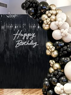 black and white balloons with happy birthday written on the wall next to it in front of a wooden floor