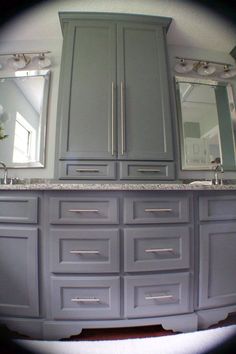 a bathroom with two sinks and large gray cabinets in front of the mirror on the wall