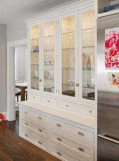 a white china cabinet with glass doors and drawers in a kitchen next to a dining room table